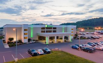 a large hotel building with a green roof and multiple parking spaces , surrounded by trees and grass at Holiday Inn Morgantown - Reading Area