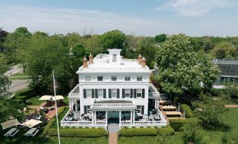 aerial view of a large white mansion surrounded by green grass and trees , with a golf course visible in the background at Topping Rose House