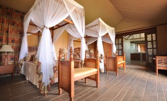 a spacious bedroom with four beds , two of which are covered by mosquito nets , and wooden furniture at Kilima Safari Camp