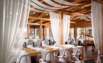 a large dining room with wooden tables and chairs , white tablecloths , and white curtains hanging from the ceiling at Bella Beach Hotel