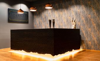 a black reception desk with a black fur - covered base is illuminated by three hanging lights and orange lights on the wall at Hotel Esplanade