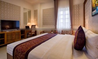 a large bed with a white and purple comforter is in the middle of a room with windows , a desk , and two chairs at Riverside Hotel Quang Binh