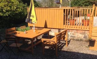 a wooden deck with multiple chairs , tables , and umbrellas , creating an outdoor dining area near a wooden fence at Loch Shiel Hotel