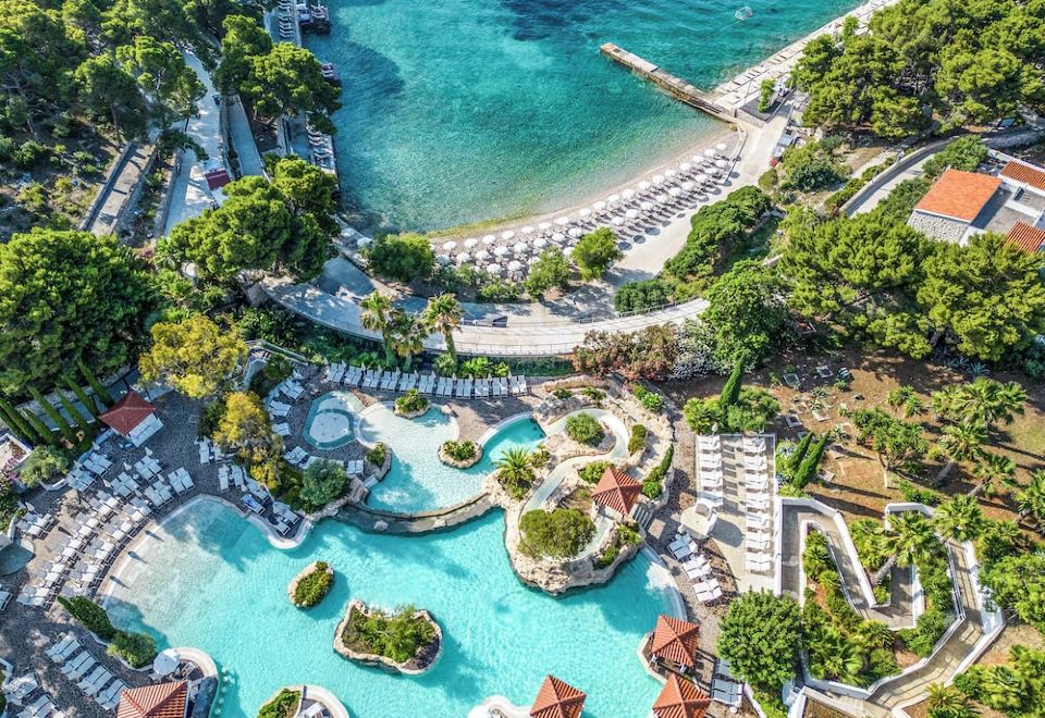 an aerial view of a resort with a pool surrounded by lush greenery and a beach at Amfora Hvar Grand Beach Resort