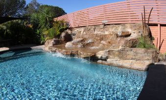 a large pool with a rock waterfall is surrounded by a stone wall and palm trees at Sleepy Hill Motor Inn