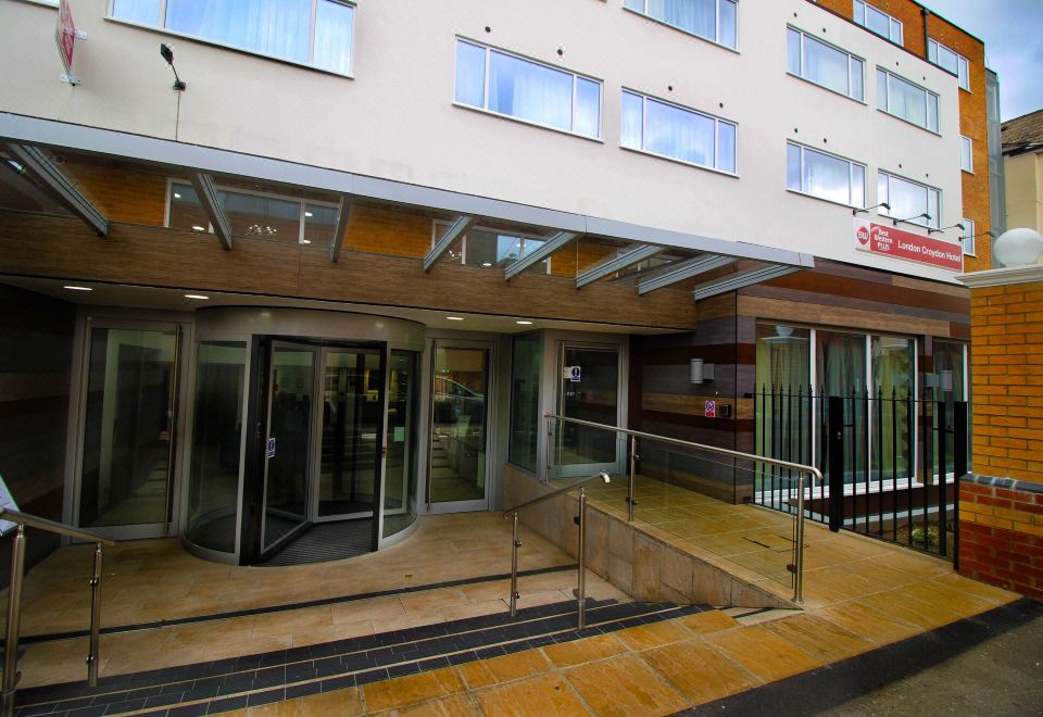 a building entrance with a metal railing , glass doors , and a wooden staircase leading up to it at Best Western Plus London Croydon Aparthotel