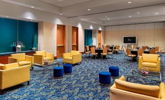 a large , well - lit room with blue and white patterned carpet , multiple couches , chairs , and tables arranged for meetings or events at Montreal Airport Marriott in-Terminal Hotel