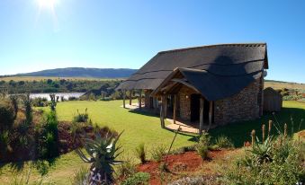a large house with a thatched roof and stone walls is surrounded by a lush green lawn at Pumba Private Game Reserve