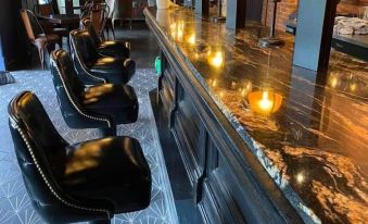 a modern bar with black leather stools , a wooden counter , and lit candles on the counter at Archer House