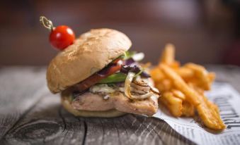 a plate with a chicken sandwich and fries , accompanied by a red cherry tomato on a wooden table at Hôtel de Glace