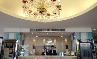 a reception area with two people behind the counter and a large chandelier hanging from the ceiling at Chaisaeng Palace Hotel