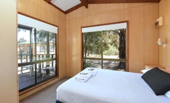 a bedroom with a large bed and white linens , overlooking a deck with a view of trees at Big4 Breeze Holiday Parks - Port Elliot