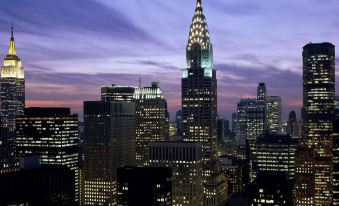 a city skyline at dusk , with the chrysler building illuminated in various colors against a purple sky at Hotel NoMa, Trademark Collection by Wyndham