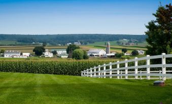 a rural landscape with a white picket fence surrounding a grassy field , and a barn in the distance at Country View PA Bed & Breakfast