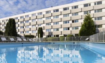 a large swimming pool is surrounded by lounge chairs and a building with many windows at Novotel Paris Nord Expo Aulnay