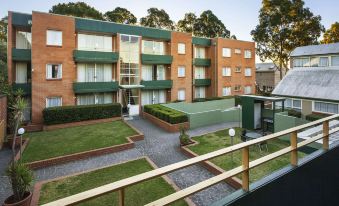 a large apartment building with multiple balconies and greenery , situated in a residential area near a grassy area at APX Parramatta