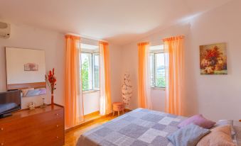 a cozy bedroom with orange curtains , wooden furniture , and a blue bedspread , bathed in sunlight at Erika