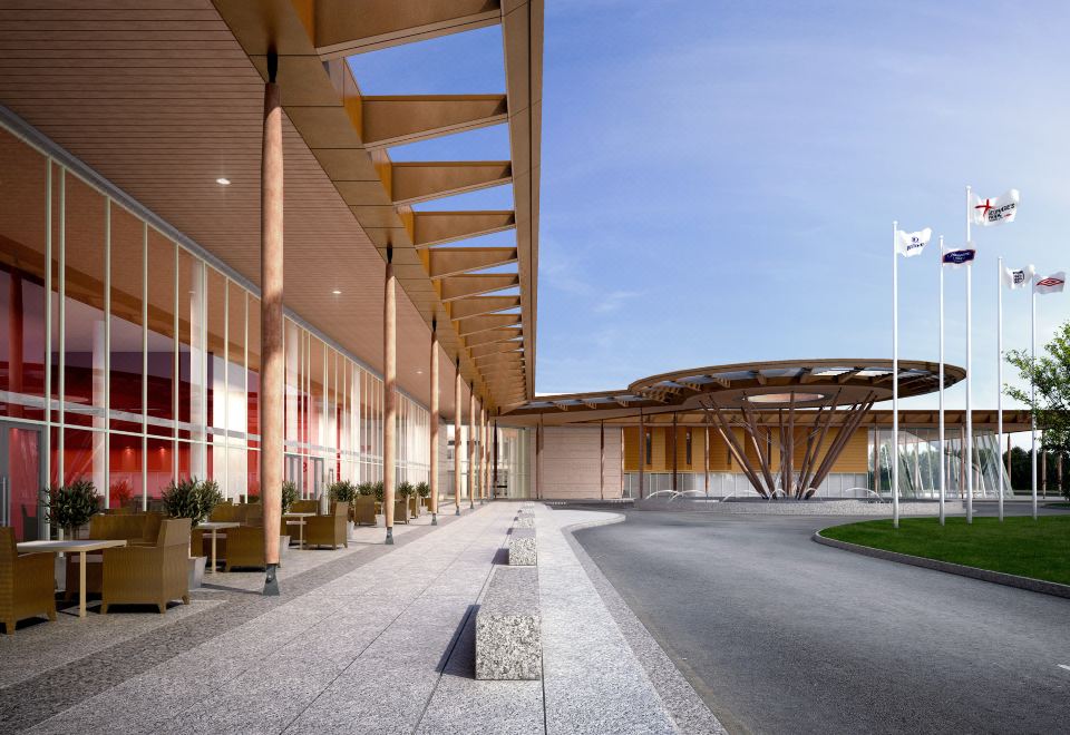 a modern building with wooden panels and large windows , surrounded by a paved walkway and flags at Hilton at St.George's Park, Burton Upon Trent