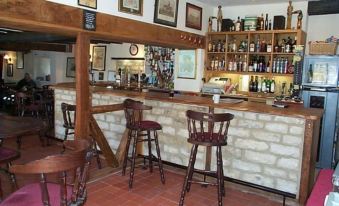 a well - decorated bar with wooden furniture , various bottles and glasses on the counter , and a brick floor at The Fox & Hounds
