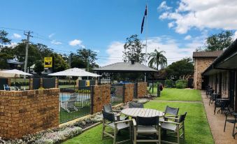 a backyard with a swimming pool surrounded by lush greenery , a dining table and chairs , and a barbecue grill at Lemon Tree Passage Motel