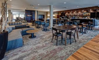 a modern lounge area with wooden tables and chairs , surrounded by bar stools and couches at Courtyard Troy