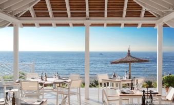 a restaurant with white tables and chairs , surrounded by a view of the ocean , under a wooden roof at Finca Cortesin Hotel Golf & Spa