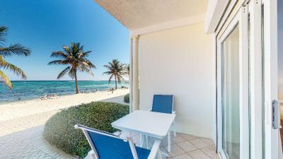 a white table and chairs are set up on a balcony overlooking the beach , with palm trees in the background at Wyndham Reef Resort Grand Cayman