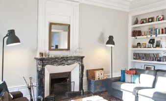 a cozy living room with a fireplace , white walls , and a wooden coffee table surrounded by books at La Grande Maison