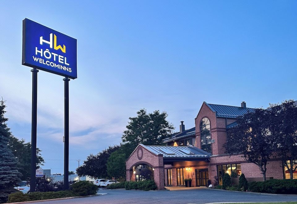 a large hotel building with a sign in front of it , surrounded by grass and trees at Hotel WelcomInns