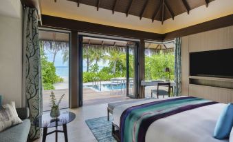 a luxurious bedroom with a king - sized bed , a television , and a view of a pool and the ocean at Pullman Maldives All-Inclusive Resort