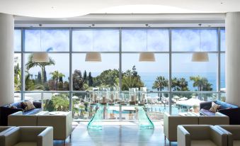 a modern hotel lobby with large windows offering a view of the ocean , including a swimming pool and lounge area at Mediterranean Beach Hotel