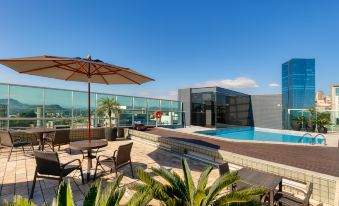 a rooftop pool surrounded by chairs and umbrellas , with a view of the city in the background at Mercure Belo Horizonte Vila da Serra
