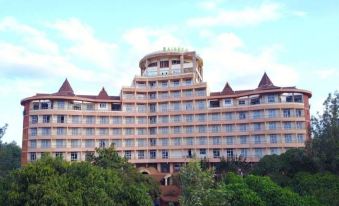 a large hotel building surrounded by trees , with the sun shining brightly in the sky at Rainbow Ruiru Resort
