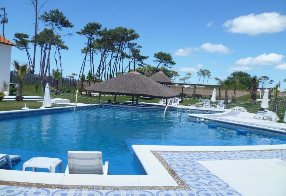 a large , rectangular swimming pool surrounded by lounge chairs and umbrellas , with a thatched - roof hut nearby at Punta del Este Arenas Hotel