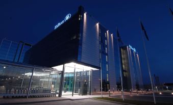 "a large hotel building with a blue sign that reads "" hilton "" is lit up at night" at Hilton Helsinki Airport