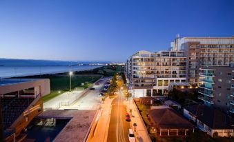 a city street at night with buildings , cars , and a body of water in the background at Sage Hotel Wollongong