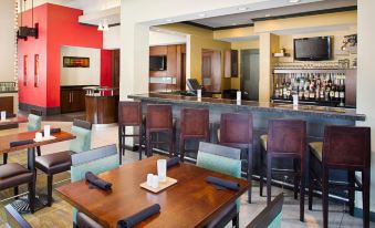 a modern restaurant with wooden tables and chairs , a bar area , and red accents on the walls at Hilton Garden Inn Albany