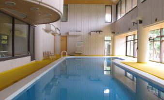 an indoor swimming pool with a yellow and blue cover , surrounded by white walls and a wooden ceiling at Wisterian Life Club Nojiriko