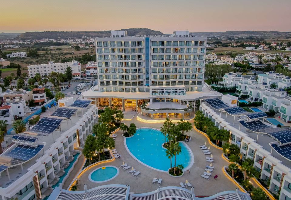 aerial view of a hotel with a swimming pool surrounded by buildings and palm trees at Radisson Beach Resort Larnaca