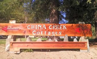 a wooden sign for china creek cottages is displayed in a park setting , surrounded by rocks and trees at China Creek Cottages