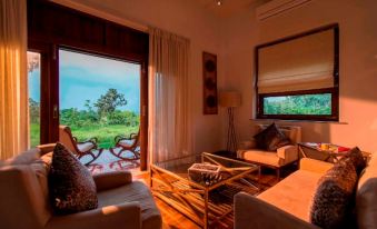 a cozy living room with two couches , a coffee table , and a door leading to a balcony overlooking a green landscape at The Serai Bandipur