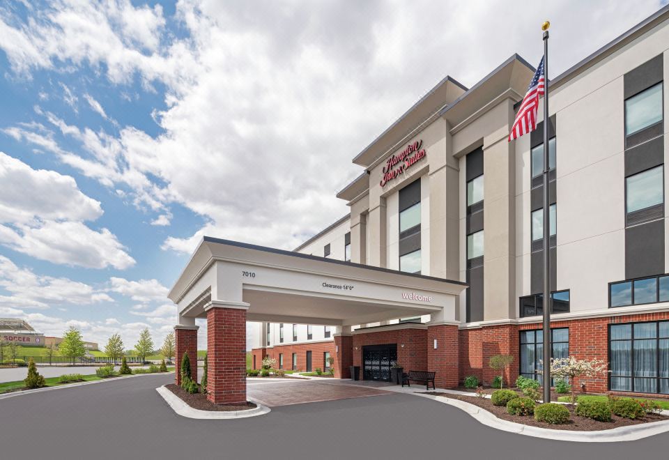 a large , modern hotel with an american flag flying above the entrance , surrounded by trees and other buildings at Hampton Inn & Suites Bridgeview Chicago