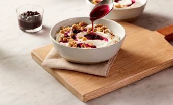 a white bowl filled with granola , yogurt , and fruit is placed on a wooden cutting board at TownePlace Suites Memphis Southaven