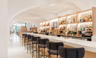 a modern bar with a long wooden counter , several stools , and a variety of bottles and glasses on the counter at Quirk Hotel Charlottesville