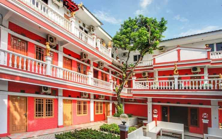 a red and white building with balconies , trees , and a large tree in front of it at Losmen Kebun Indah