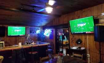 a cozy bar with wooden walls , two large tvs mounted on the wall , and a pool table at RiverBend Lodge