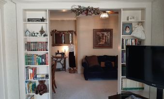 a living room with a couch , television , and bookshelves filled with books is shown through an open doorway at Barclay Bed and Breakfast