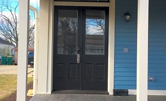 a black front door of a blue house with a white porch , surrounded by greenery at The Plainfield Inn