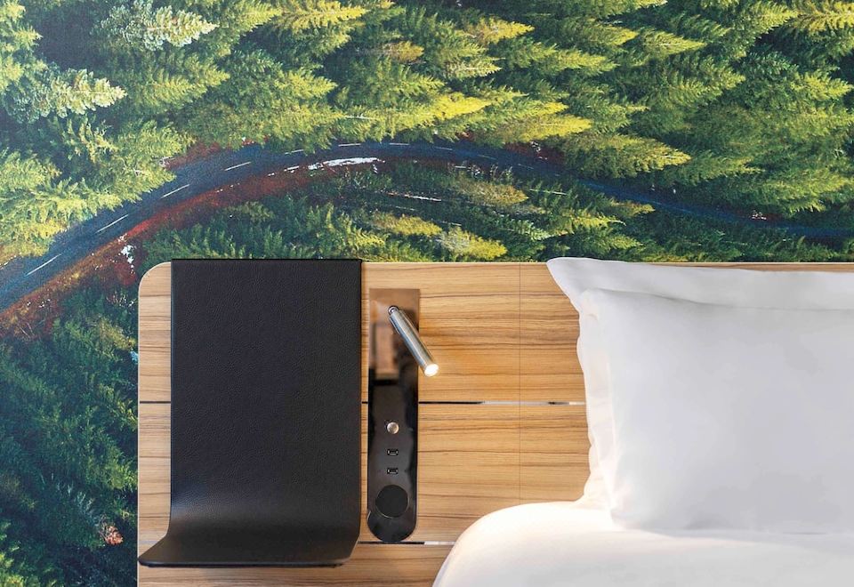 a bed with a headboard and white sheets is next to a wooden nightstand with a black lamp at Novotel Marne-la-Vallée Noisy-Le-Grand