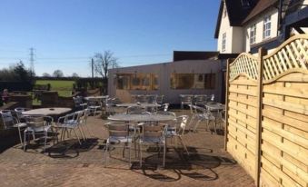 a brick patio with several tables and chairs set up for outdoor dining , surrounded by a wooden fence and a building at Rettendon Lodge